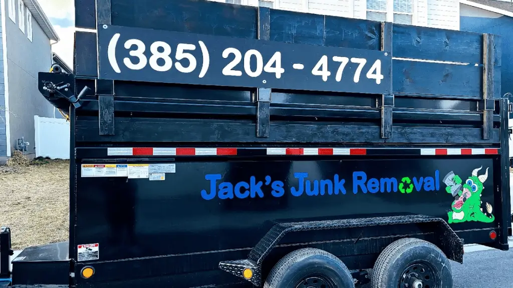 A black dumpster trailer with a phone number on top and blue text “Jack’s Junk Removal” with a cartoon green mascot on the side.